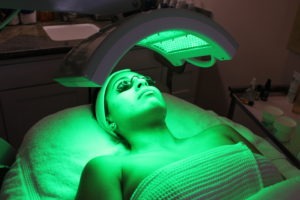 A woman is getting her skin cleaned by the green light.
