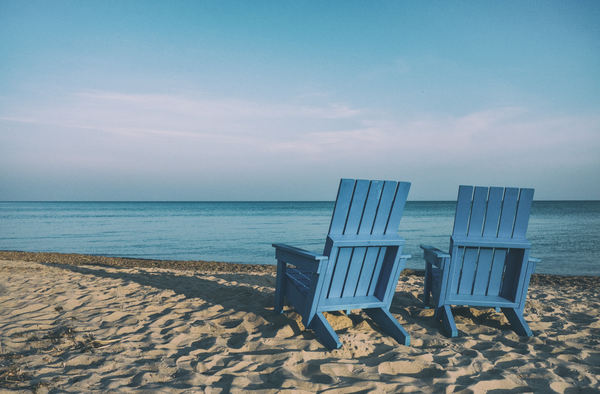 Two blue chairs on the beach near water