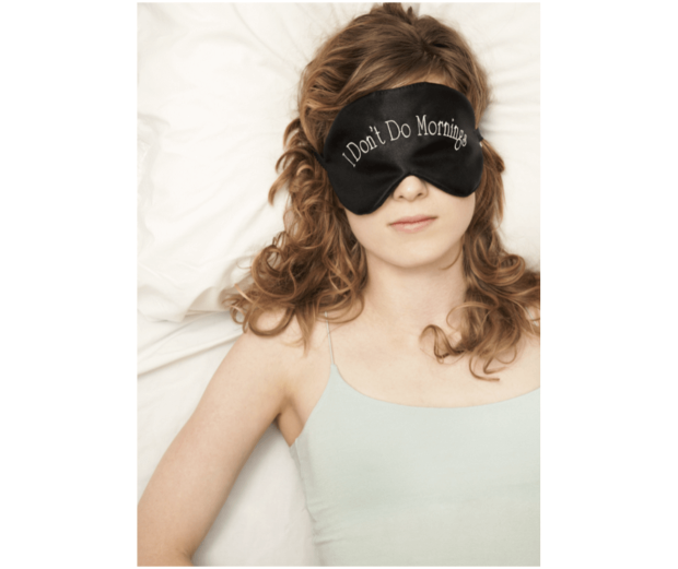 A woman laying in bed with a black eye mask on.